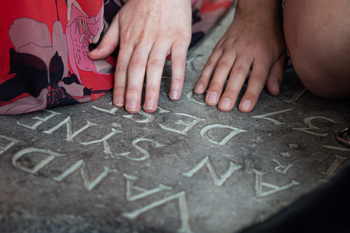 Op deze foto zijn handen van dichtbij te zien. De handen voelen aan een inscriptie op een van de grafstenen die verwerkt zijn in de vloer van de Grote Kerk Breda.