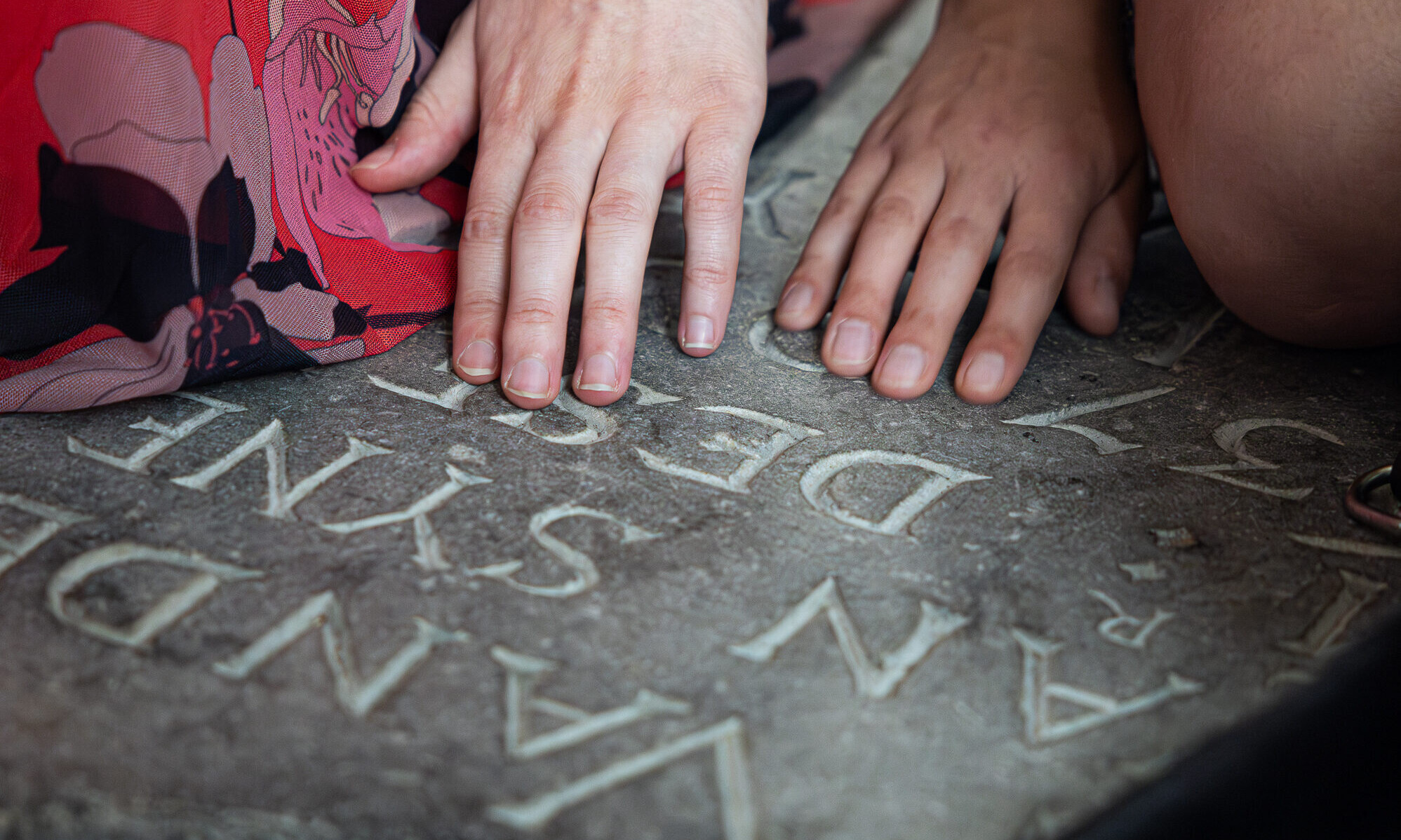 Op deze foto zijn handen van dichtbij te zien. De handen voelen aan een inscriptie op een van de grafstenen die verwerkt zijn in de vloer van de Grote Kerk Breda.